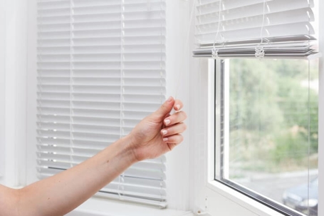 Homeowner closing their blinds to save on energy bills